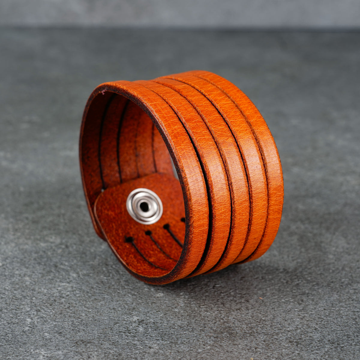 Angled product view highlighting the curved cuff shape and layered orange leather