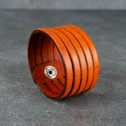 Angled product view highlighting the curved cuff shape and layered orange leather