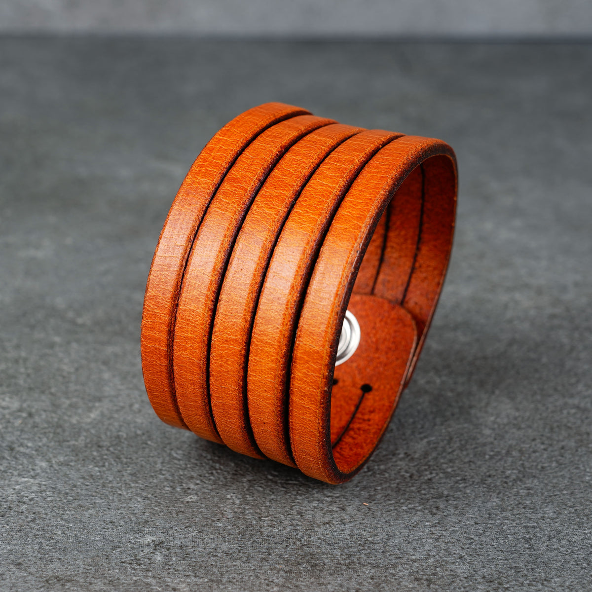 Orange leather cuff bracelet shown on a wrist from a side angle