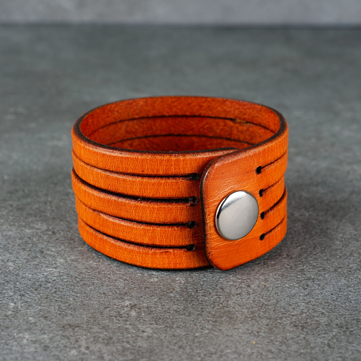 Orange leather cuff bracelet with a visible metal snap from the front