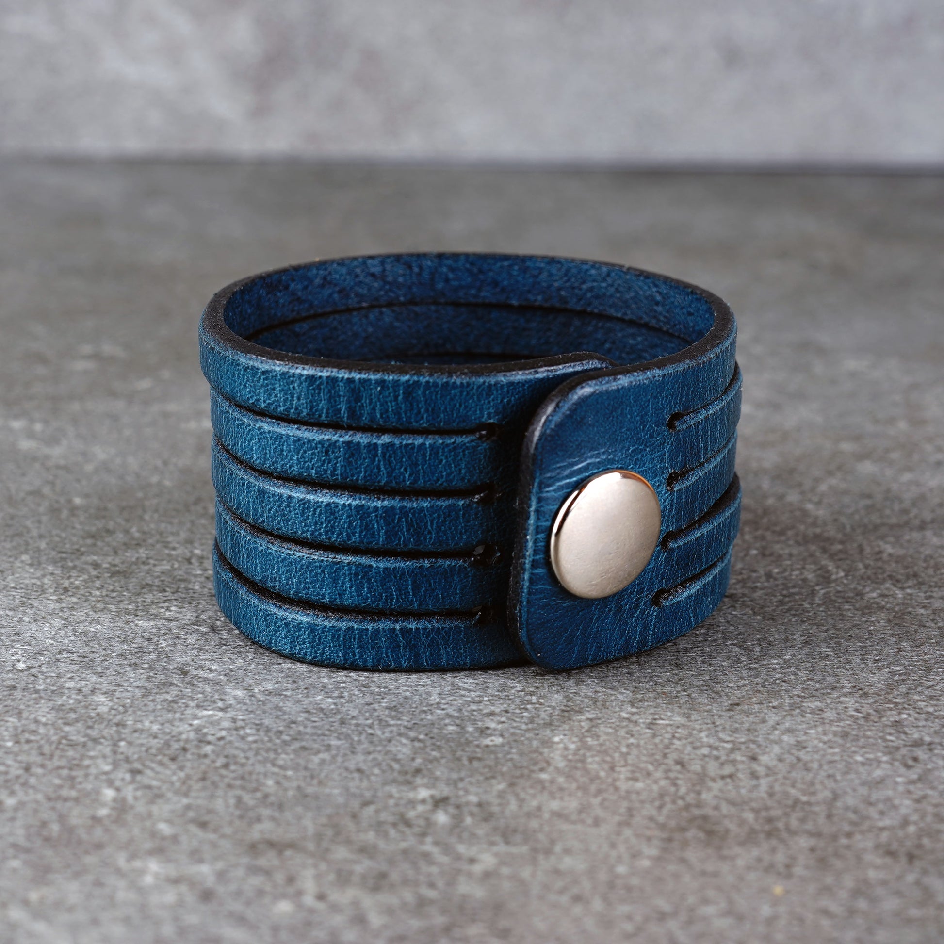 Blue leather wrap bracelet on gray background, handmade genuine leather cuff bracelet with layered strap design, minimalist blue wristband accessory for men and women
