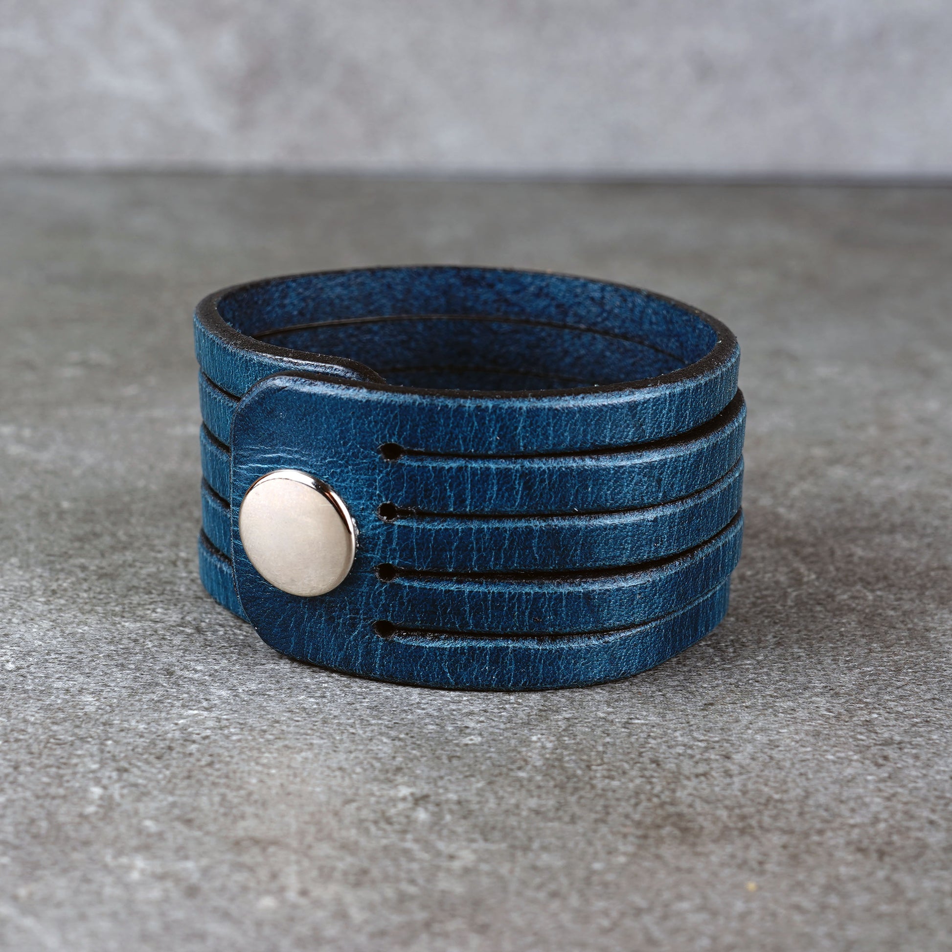 Blue leather wrap bracelet on gray background, handmade genuine leather cuff bracelet with layered strap design, minimalist blue wristband accessory for men and women
