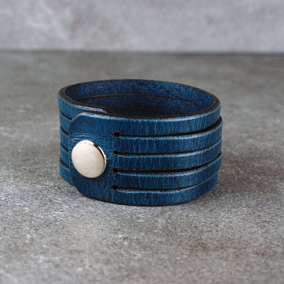Blue leather wrap bracelet on gray background, handmade genuine leather cuff bracelet with layered strap design, minimalist blue wristband accessory for men and women
