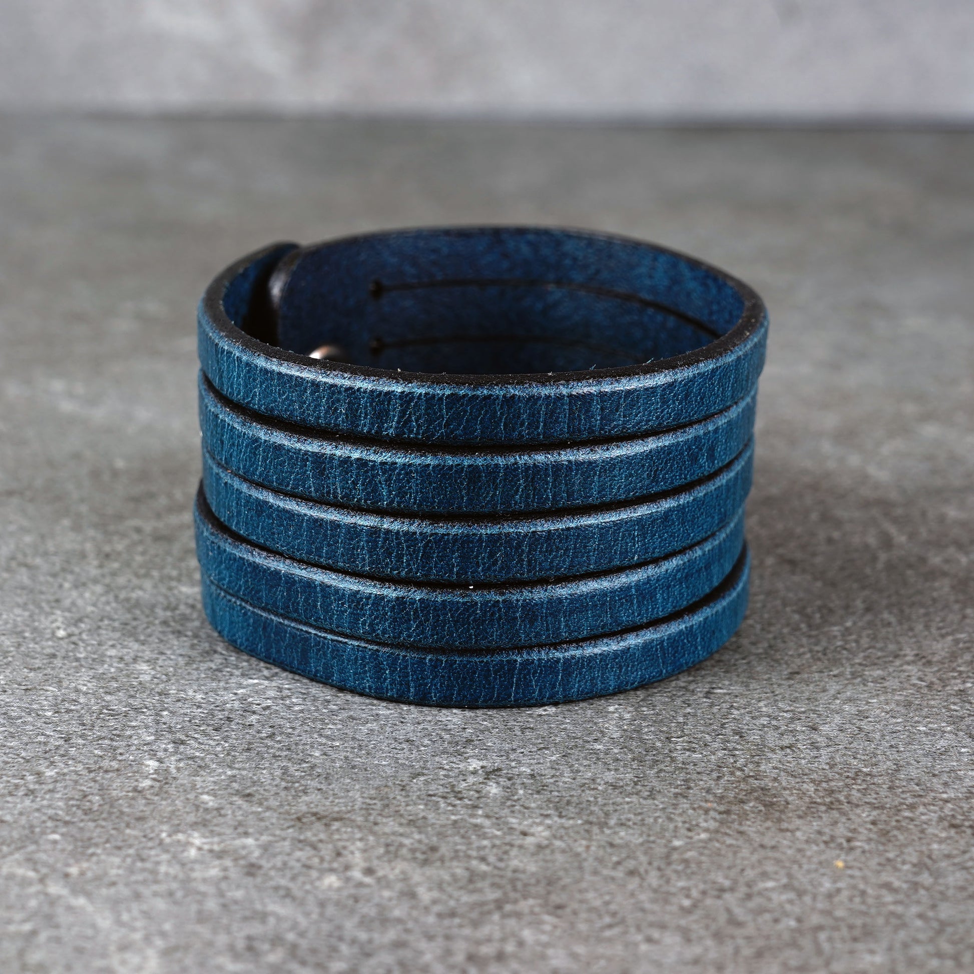 Blue leather wrap bracelet on gray background, handmade genuine leather cuff bracelet with layered strap design, minimalist blue wristband accessory for men and women
