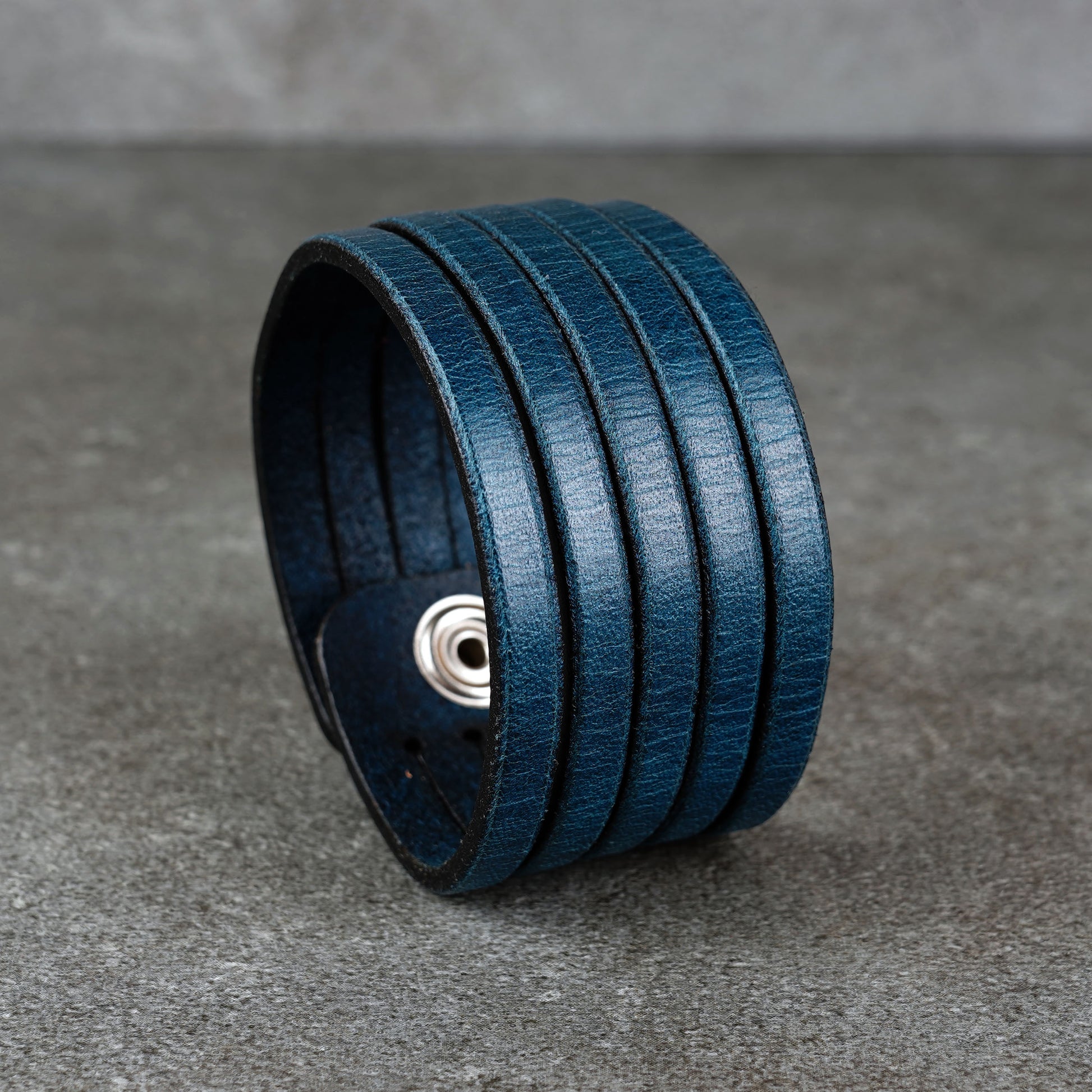 Blue leather wrap bracelet on gray background, handmade genuine leather cuff bracelet with layered strap design, minimalist blue wristband accessory for men and women
