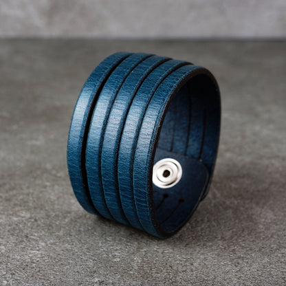 Blue leather wrap bracelet on gray background, handmade genuine leather cuff bracelet with layered strap design, minimalist blue wristband accessory for men and women
