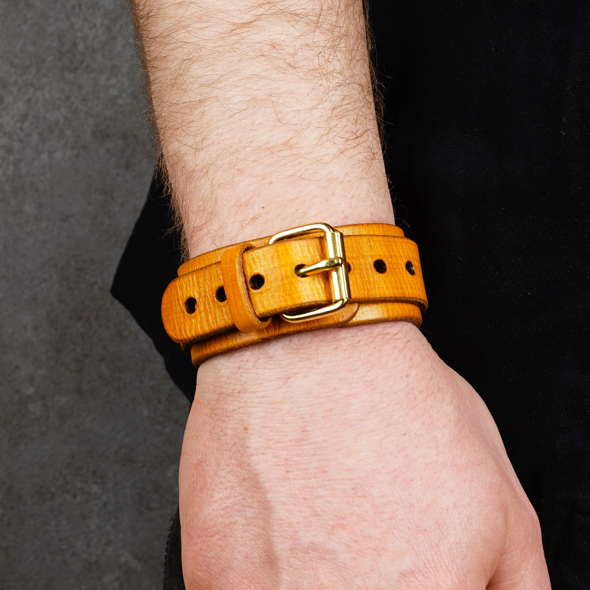 Yellow leather cuff bracelet on a wrist, with a brass buckle and punched holes visible.