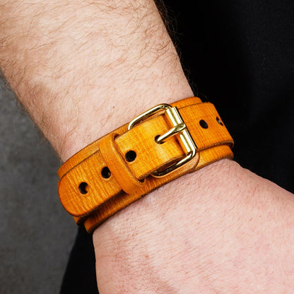 Yellow leather cuff bracelet with a brass buckle on a wrist, shown angled with punched holes visible.