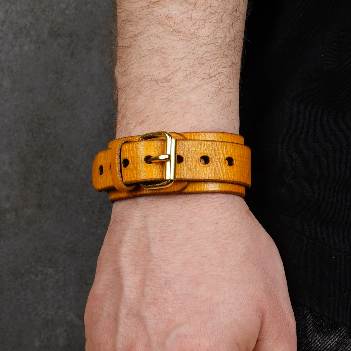 Yellow leather cuff bracelet worn on a wrist, shown with a brass buckle and punched holes.
