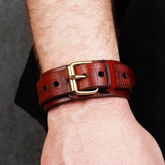 Brown leather cuff bracelet worn on a wrist with a brass buckle and punched holes
