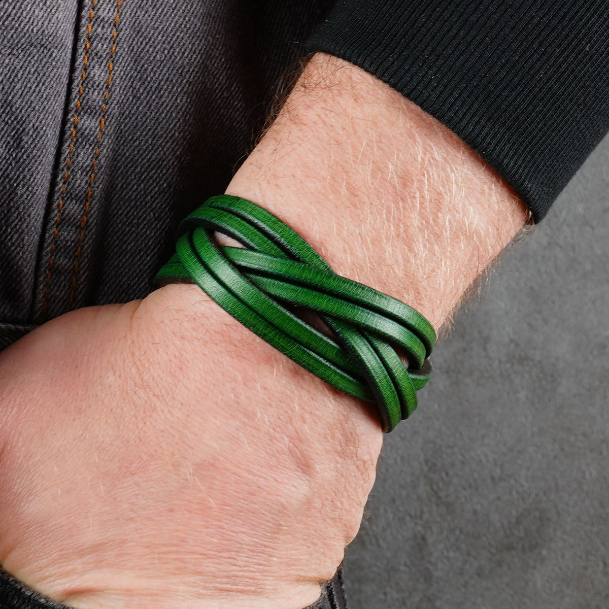 Green woven leather bracelet worn on a wrist beside dark clothing