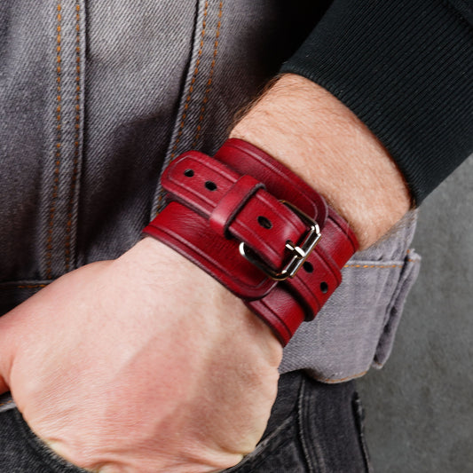 Red leather cuff bracelet on a wrist, angled side view, with a metal buckle, strap holes, and snap fasteners.