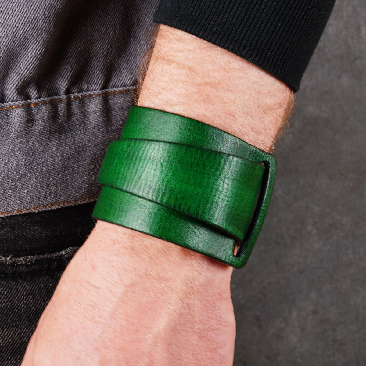 Green leather cuff bracelet worn near denim and a dark sleeve