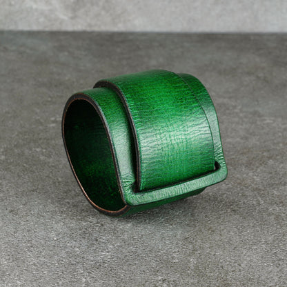Curved green leather cuff standing upright on a gray surface