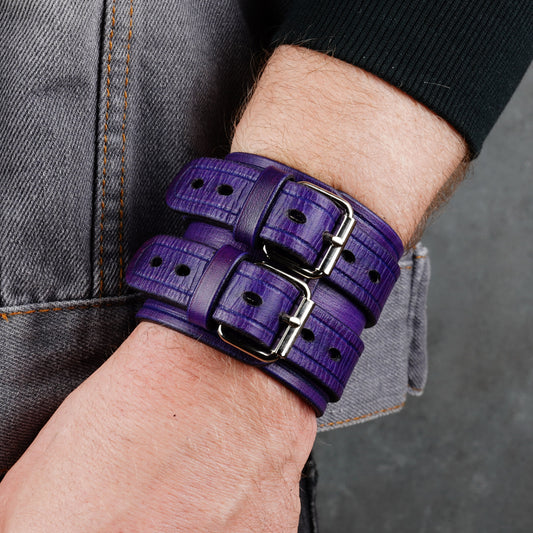 Purple leather cuff bracelet worn on a wrist with two buckle straps and visible metal rivets