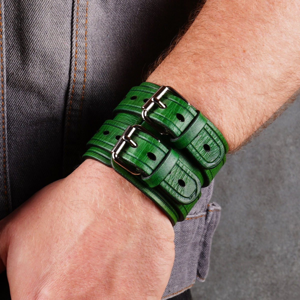Green leather cuff bracelet on a wrist with the buckle and punched holes visible