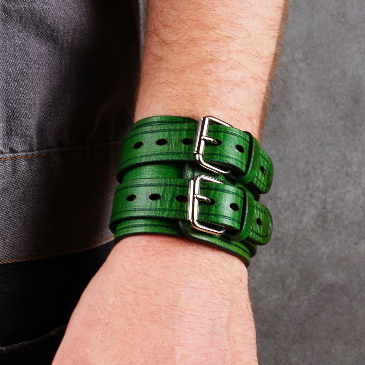 Two green leather cuff bracelets worn together with visible buckles and punched holes