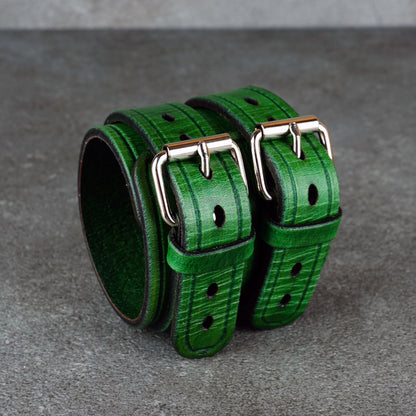 Pair of green leather cuffs displayed side by side with rounded buckle hardware