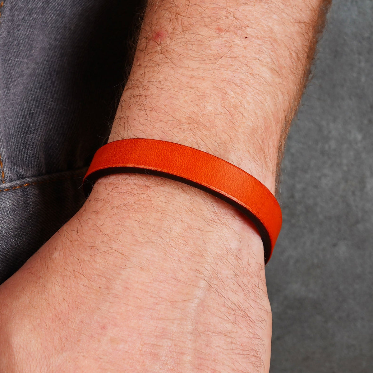 Bright orange leather bracelet worn on a wrist, shown without the clasp visible.