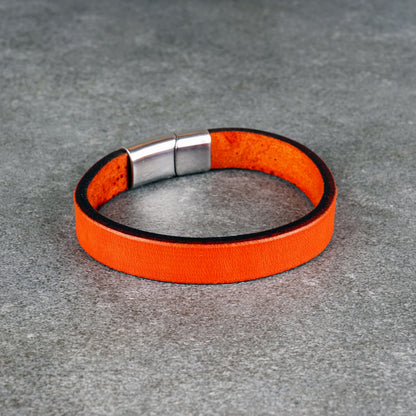 Orange leather bracelet laid in a circle on a gray surface, with a silver metal clasp at the top.