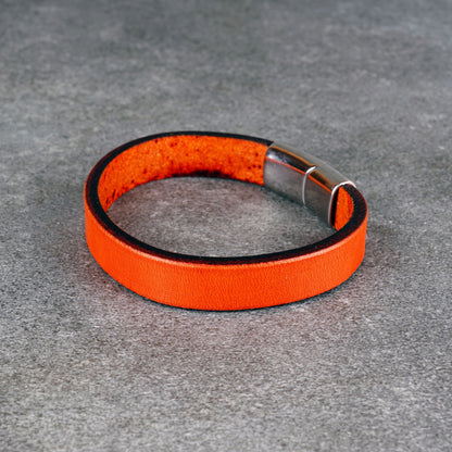 Orange leather bracelet laid in a circle on a gray surface, with a silver metal clasp at one side.